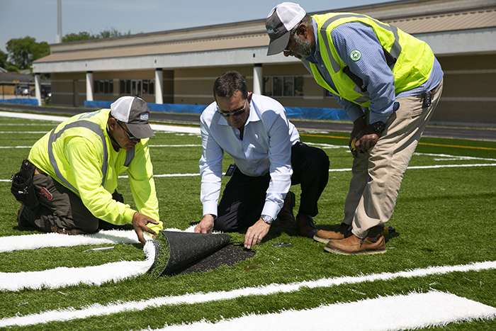Hellas President and CEO Reed J. Seaton works with Salvador Martinez and Superintendent Saleh Khan to inlay yardage numbers on a Hellas Matrix® Helix field with Cushdrain® pad being installed at Dement Field in Galena Park, Texas on Tuesday.